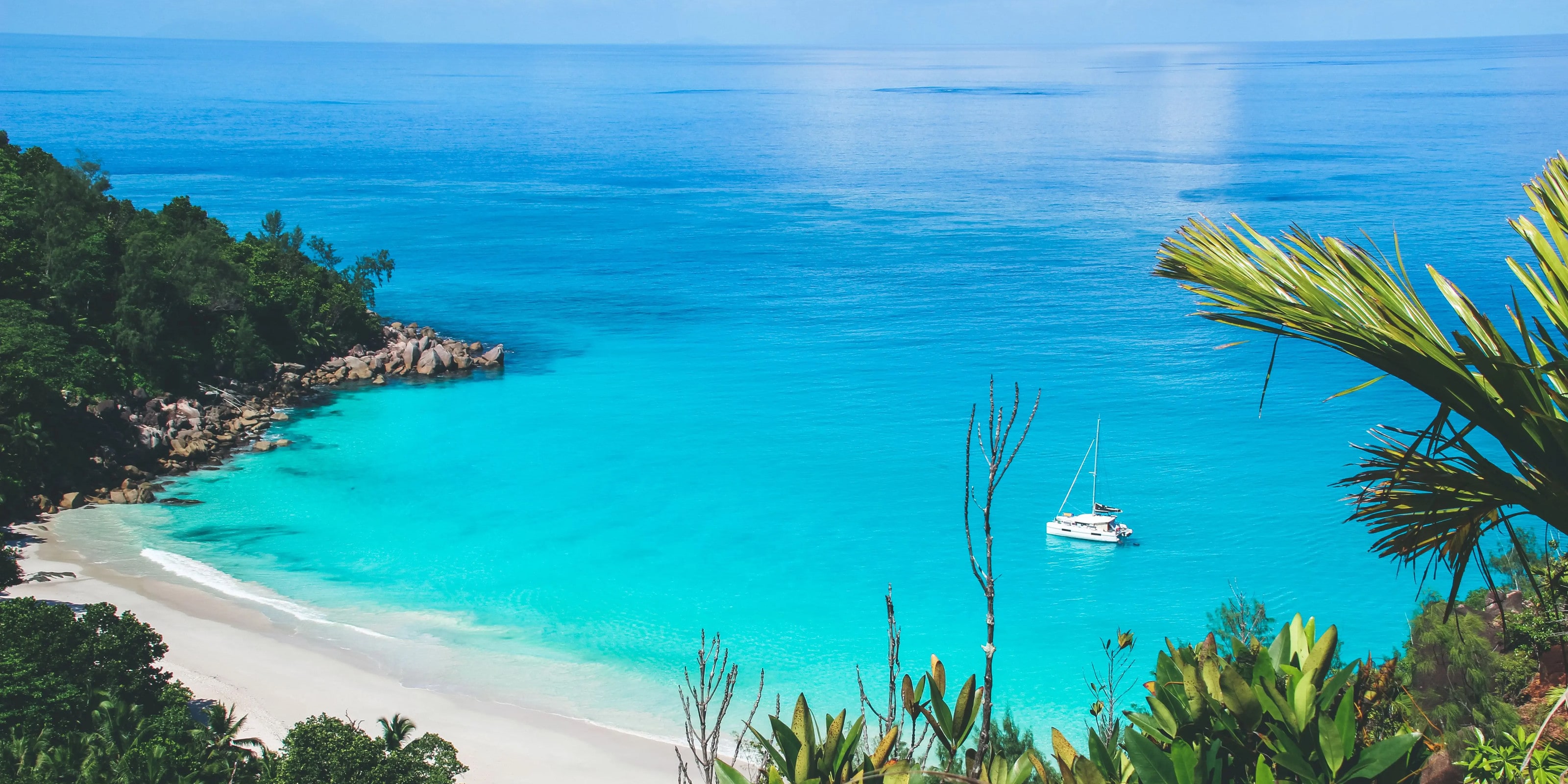 A turquoise bay with white sand, granite headland and a moored yacht